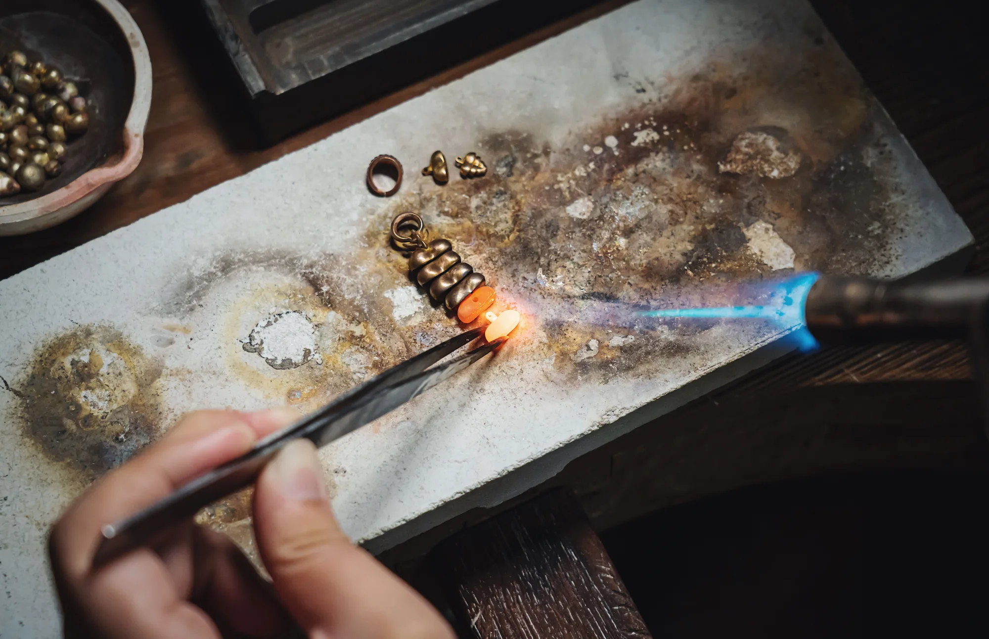 Goldschmied erhitzt kleine Metallteile mit einem Brenner