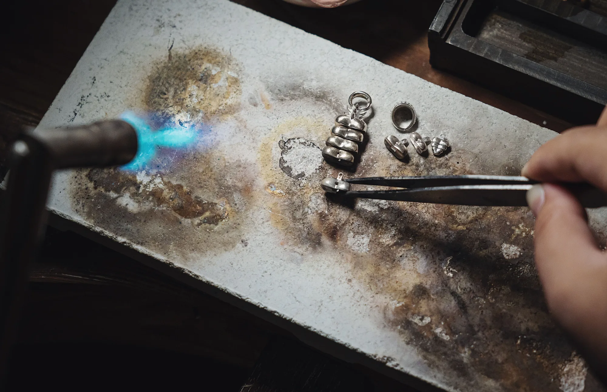 Ein Silberschmied bearbeitet Schmuck mit einer Flamme in der Werkstatt.