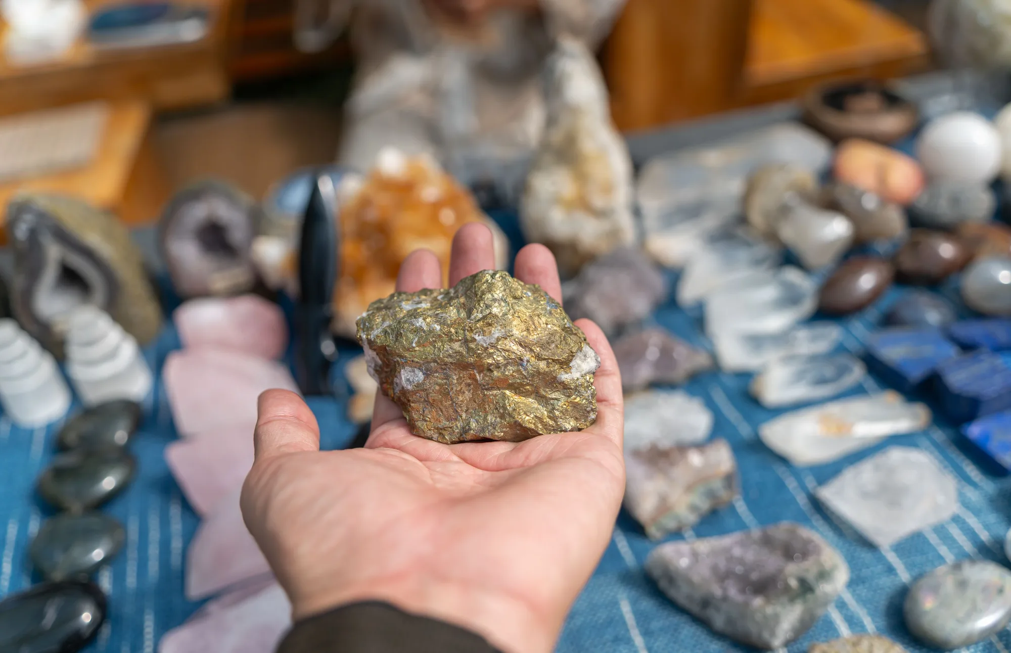 Eine Hand hält ein Rohmineral vor weiteren Steinen