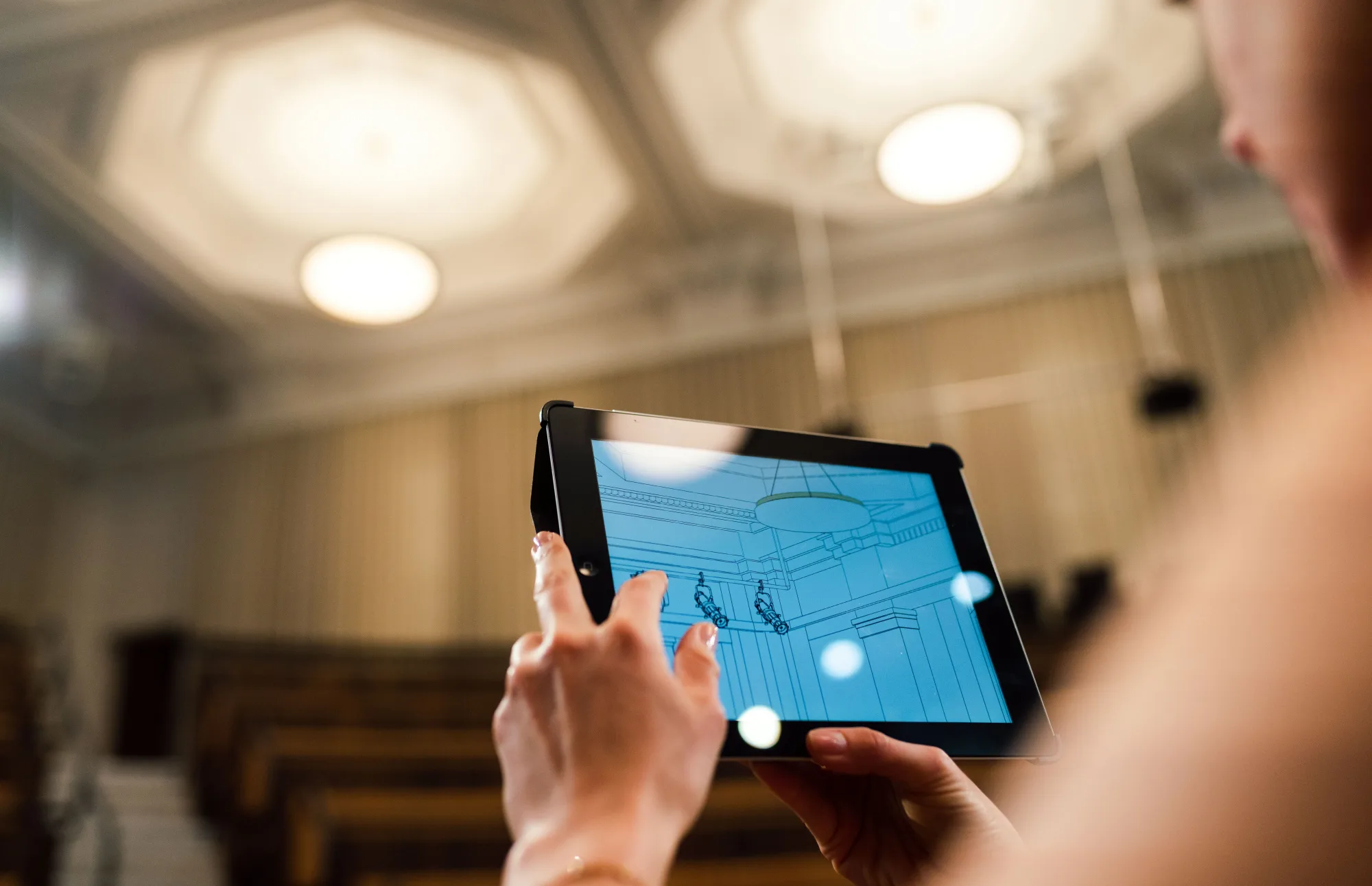 Eine Ingenieurin analysiert auf einem Tablet die Technik eines großen Innenraums.