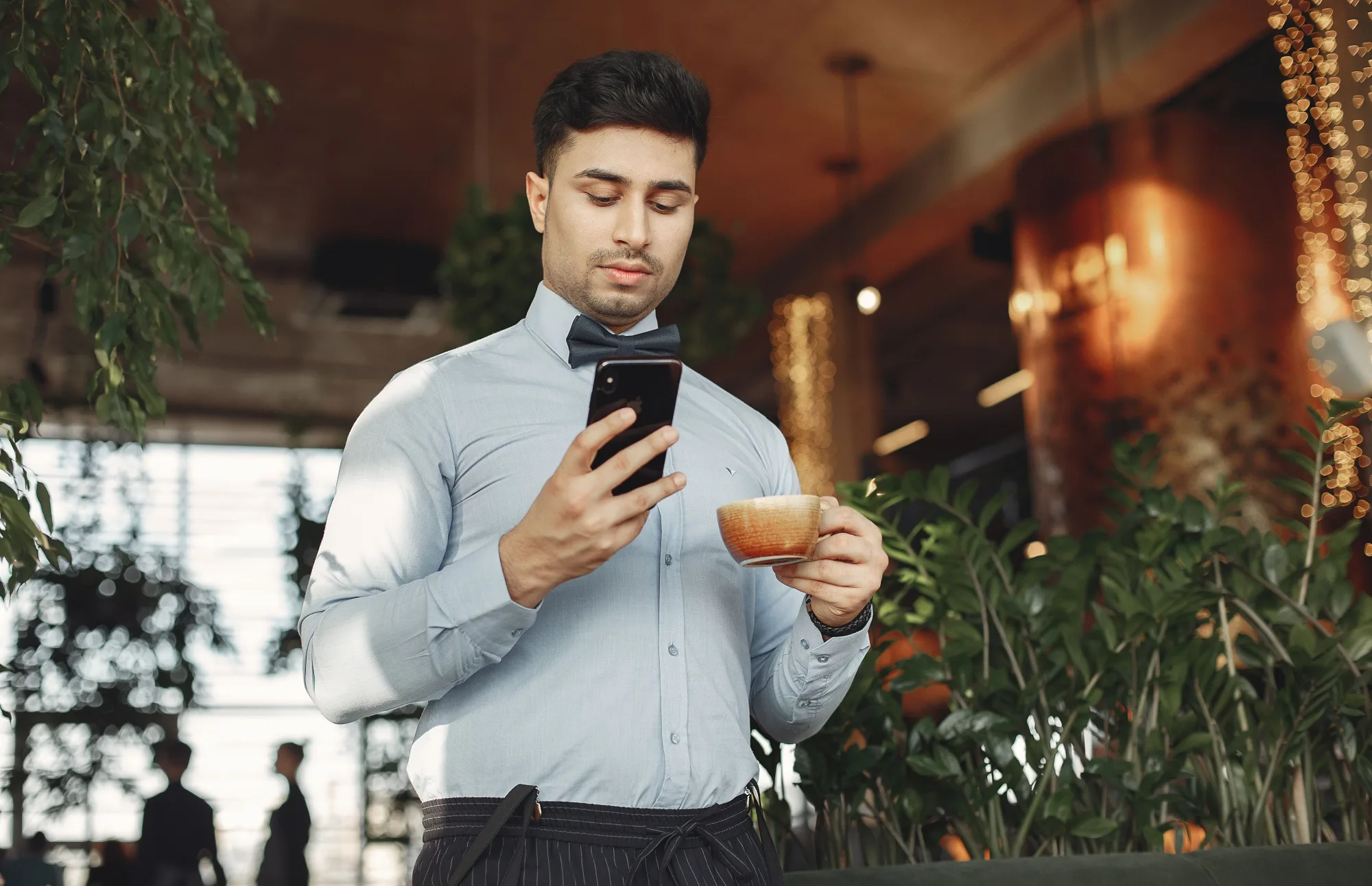 Junger Mann prüft sein Smartphone bei einer Tasse Kaffee im Café