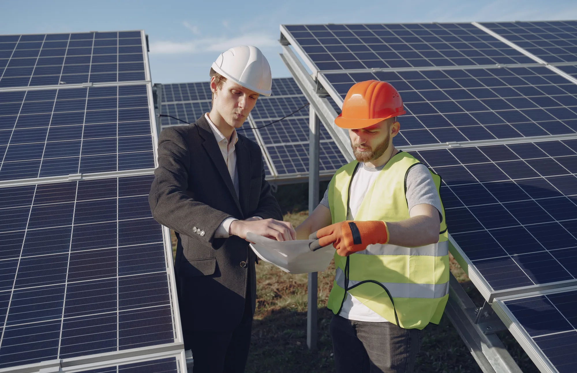 Zwei Fachleute prüfen Unterlagen zwischen Solarmodulen.