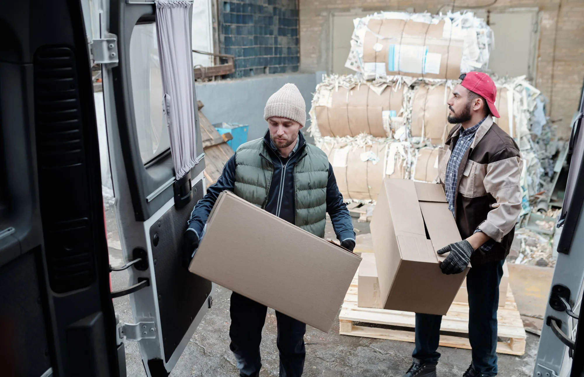 Zwei Lagerarbeiter transportieren Kartons vor gepresstem Altpapier