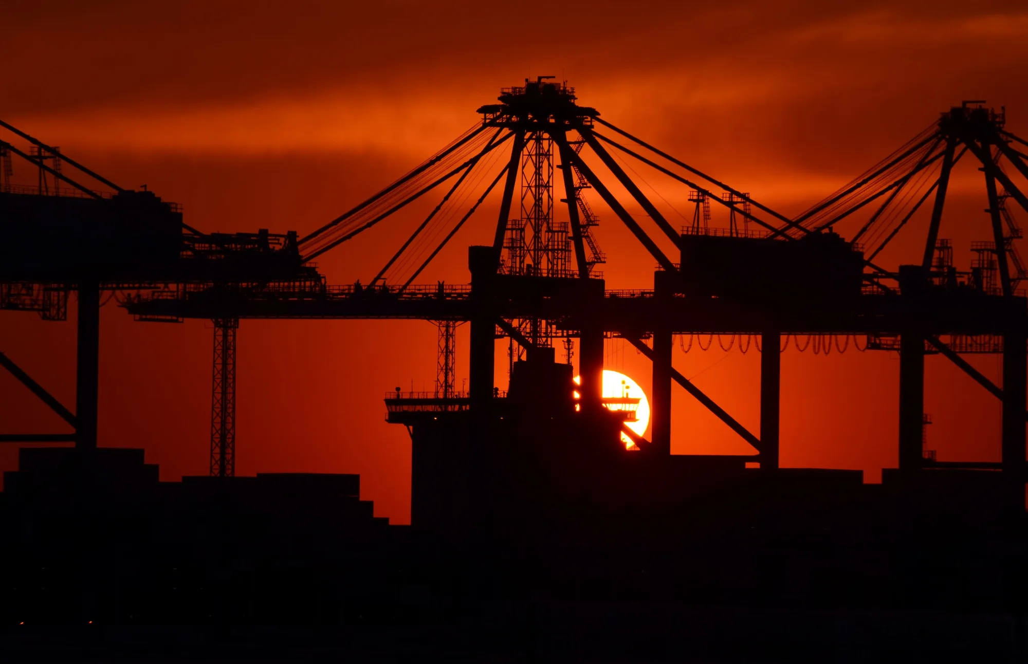 Containerkräne zeichnen sich als Silhouetten vor dem Abendhimmel ab