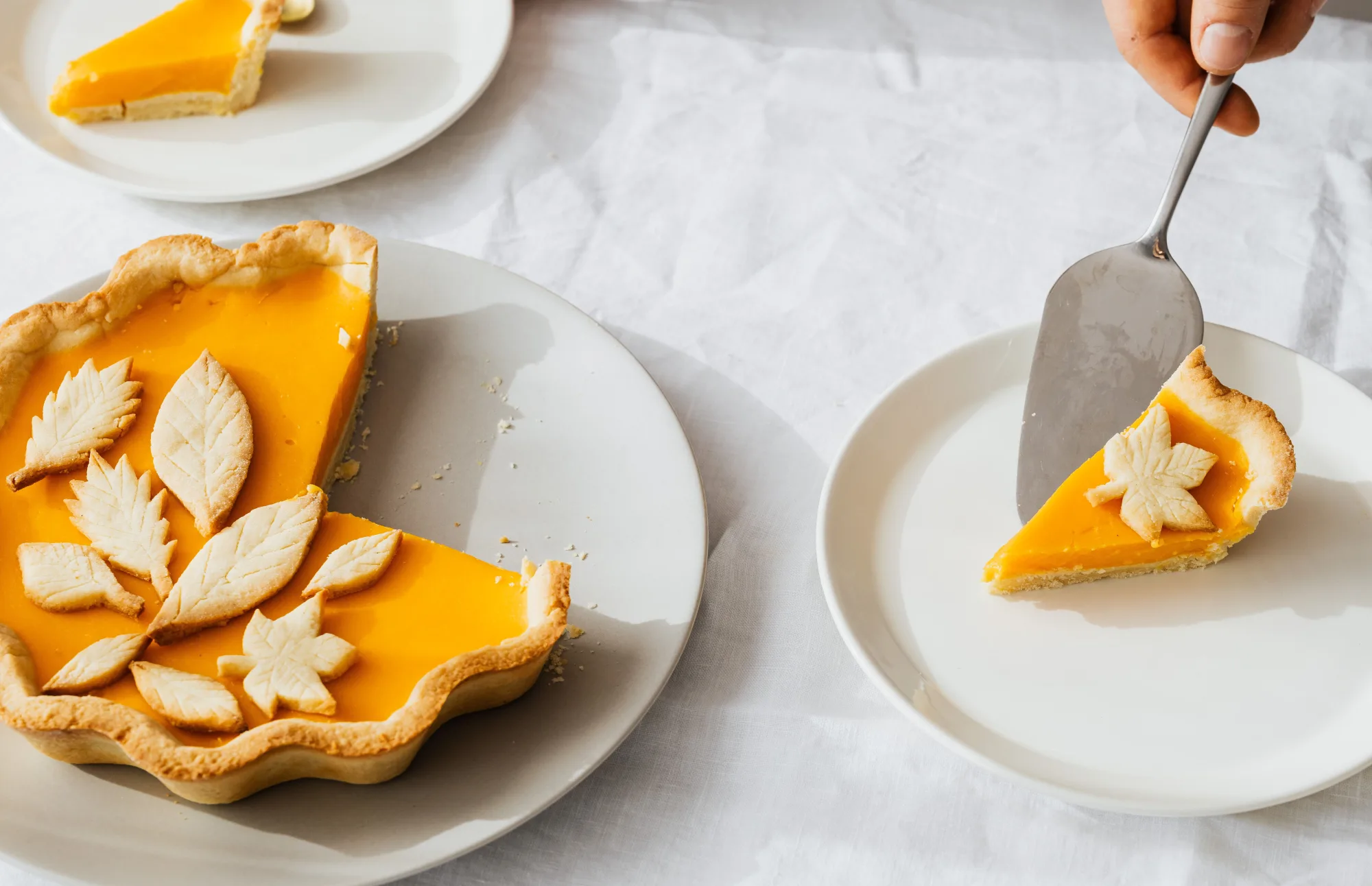 Eine Hand serviert ein Stück Kürbiskuchen von einem angeschnittenen Kuchen