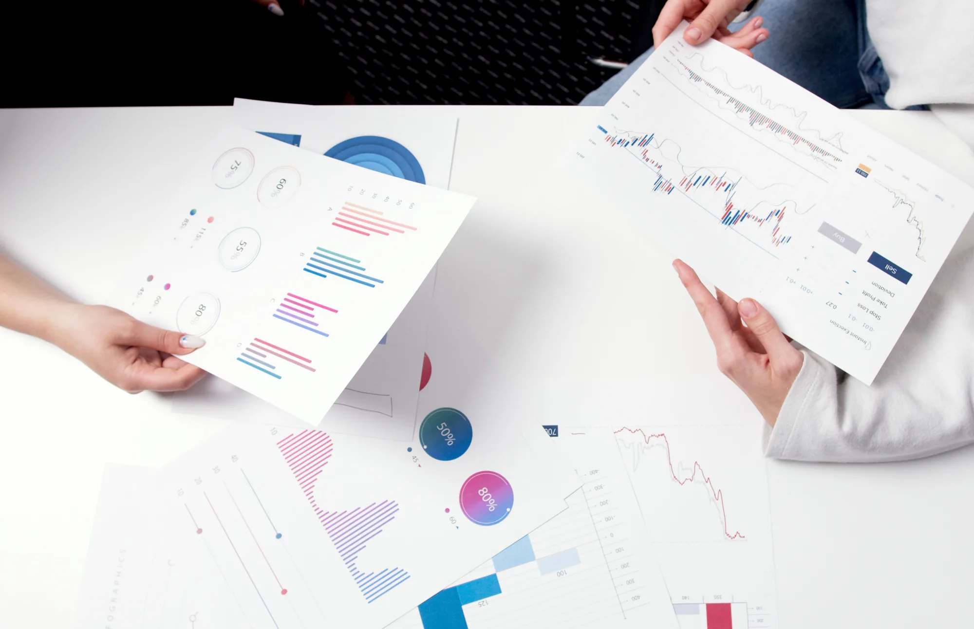 Hände vergleichen Finanzdiagramme und Marktberichte bei einer Besprechung