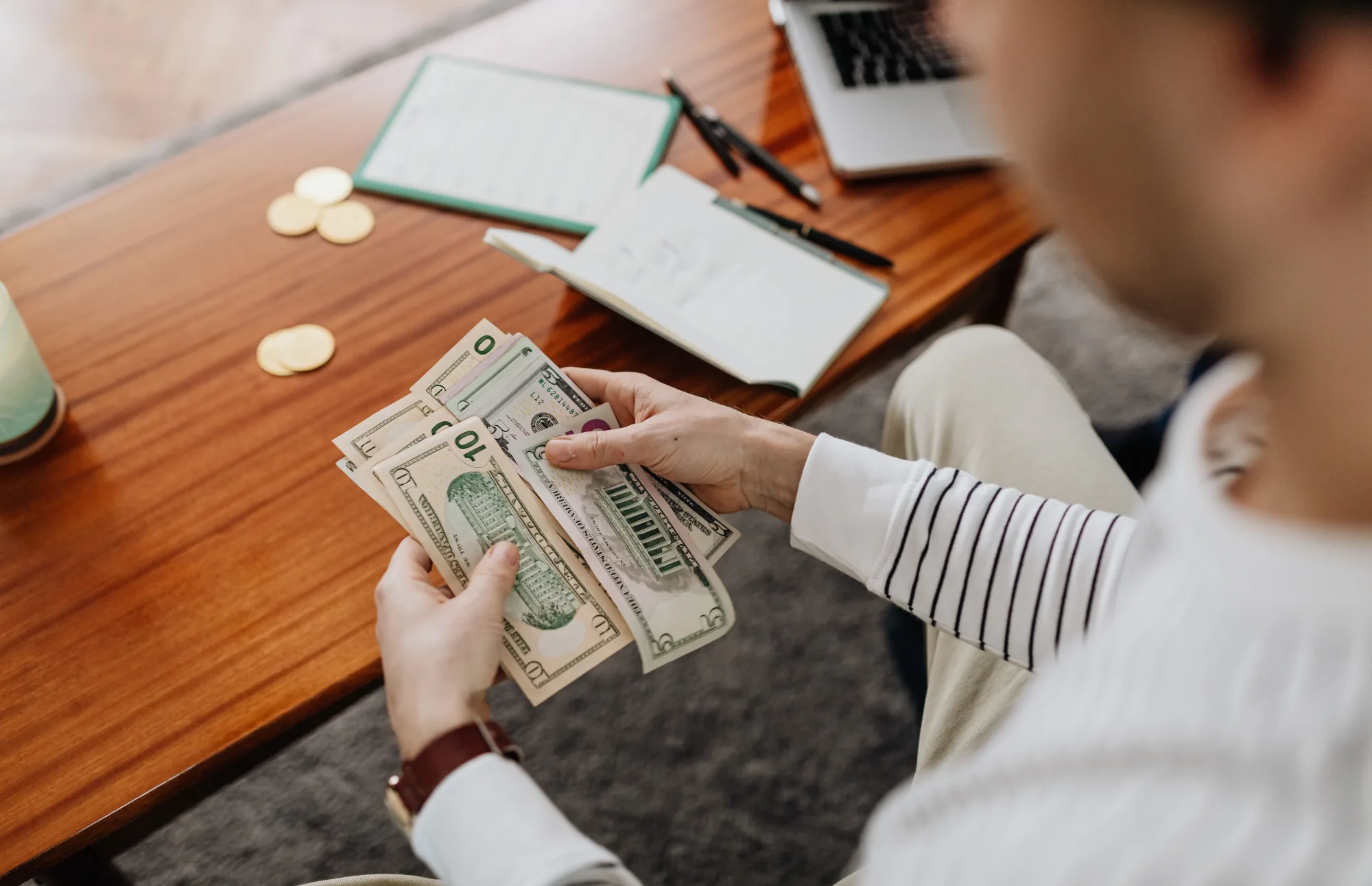 Eine Person zählt US-Dollar-Scheine neben Notizen und Münzen.