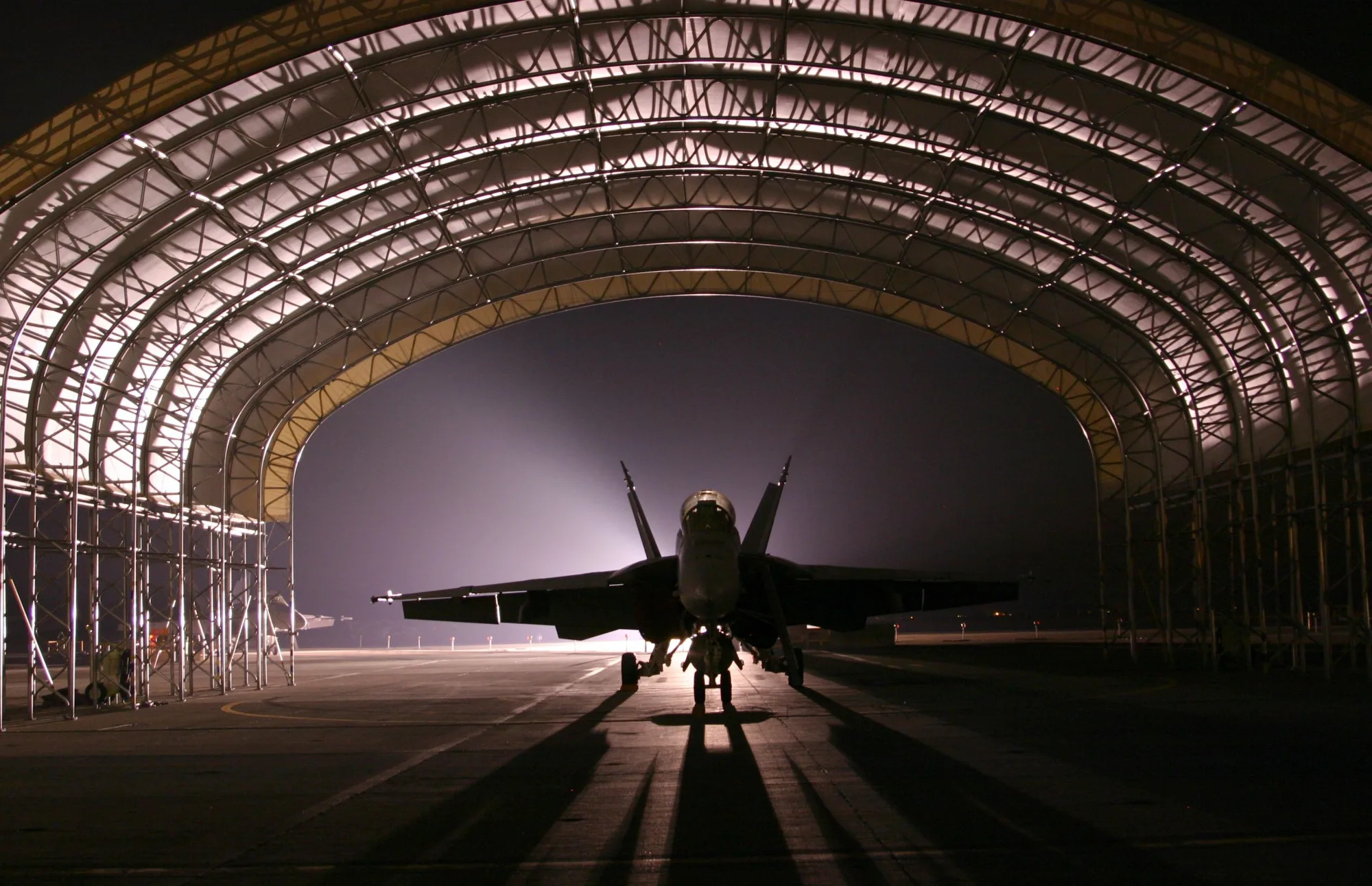 Ein Kampfflugzeug steht als Silhouette in einem Hangar