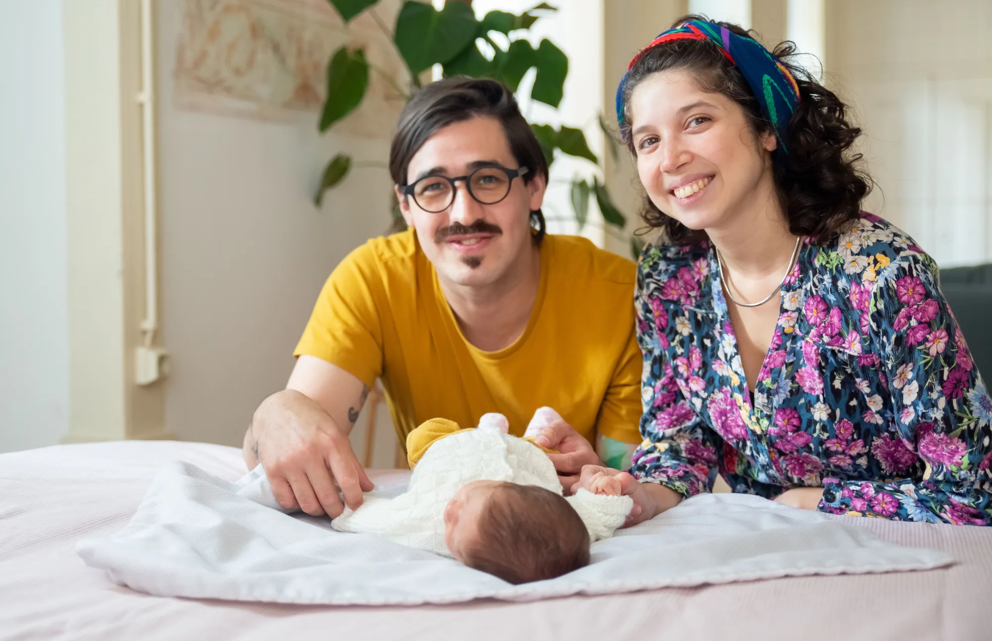 Junge Eltern liegen mit ihrem Baby auf dem Bett und lächeln.