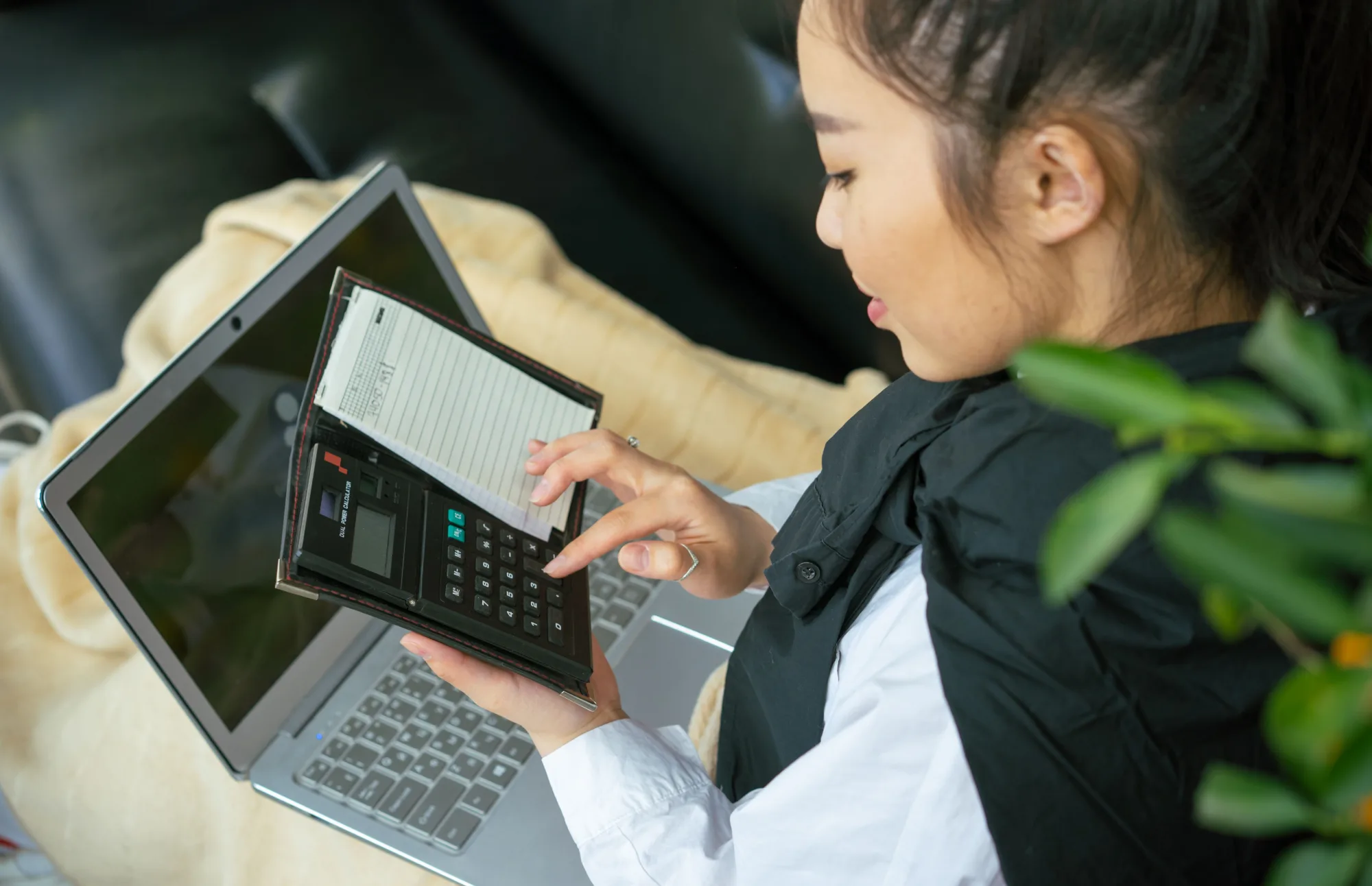 Eine junge Frau plant ihre Finanzen mit Laptop und Taschenrechner.