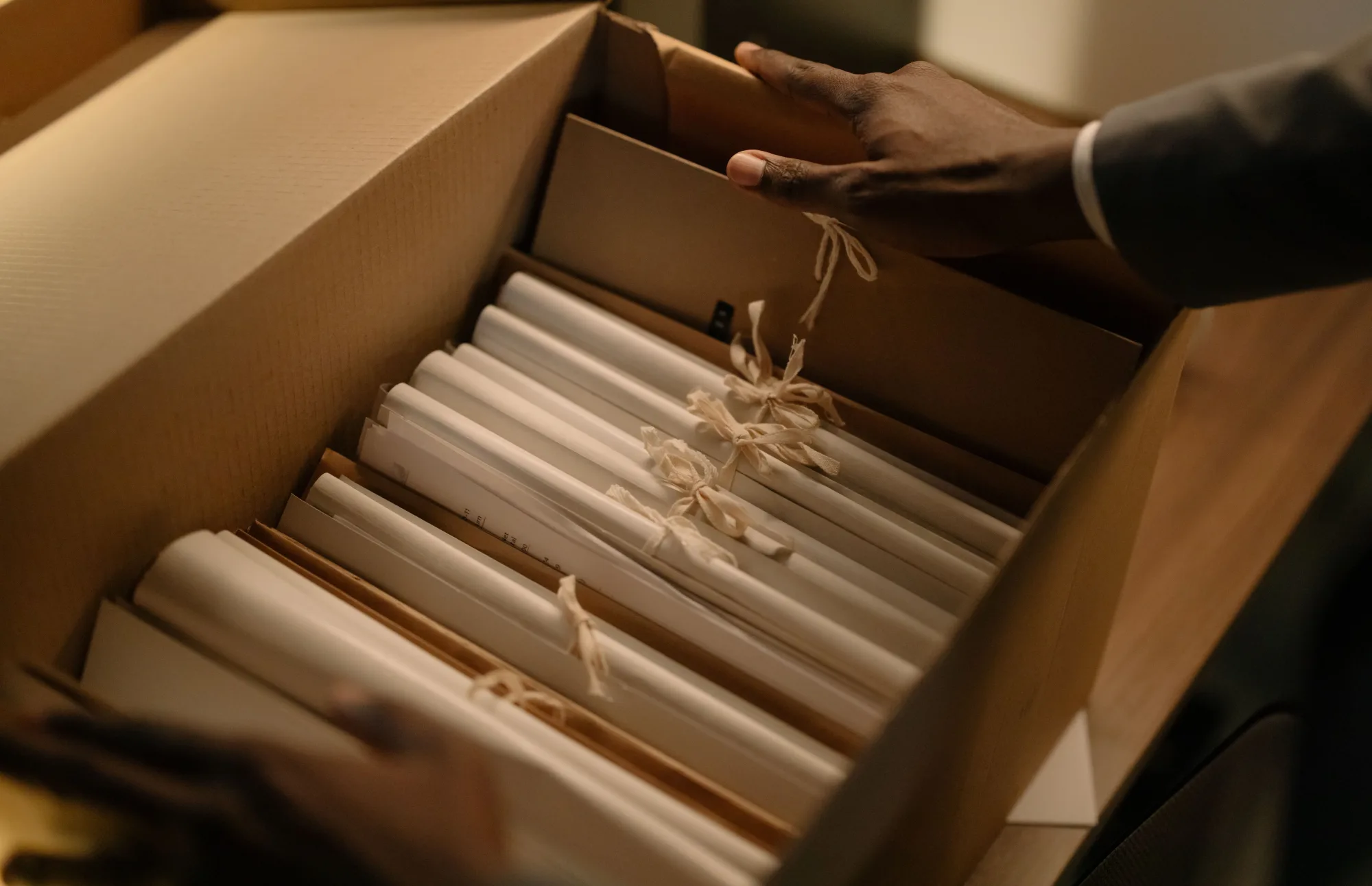 Hände ordnen gebündelte Dokumente in einem Archivkarton